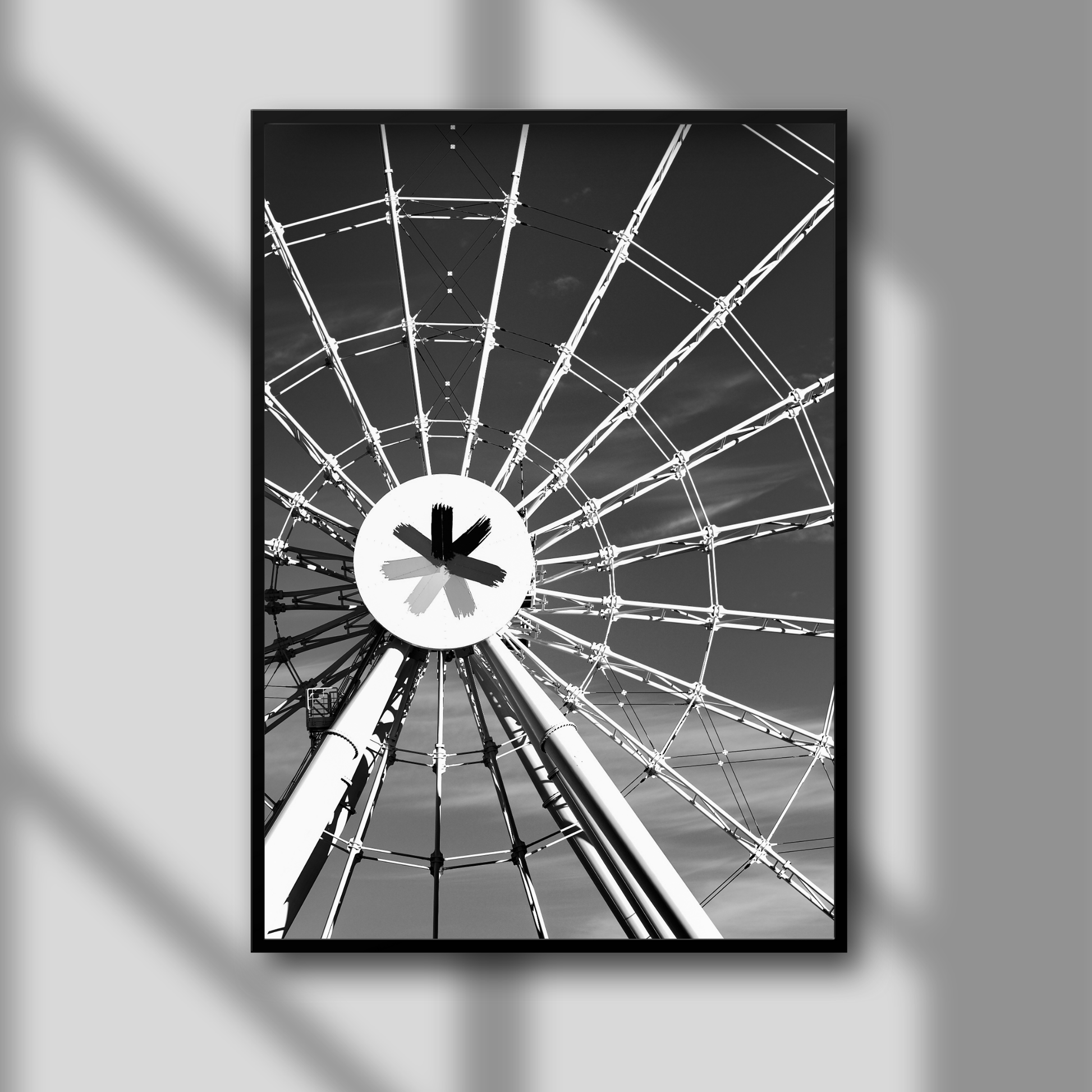 A framed black and white photograph of a Ferris wheel, with a solid black frame and a glass overlay, hanging on a white wall.