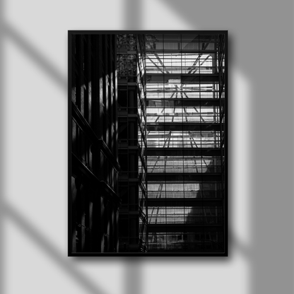 A framed black and white photograph of shadow lines cast by a glass skywalk on a building, with a solid black frame and a clear glass overlay.