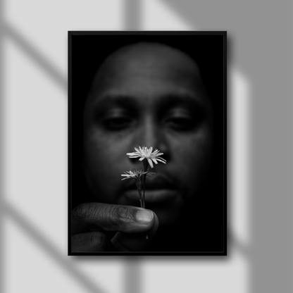 A black and white photograph of a person holding a small flower, framed in black with a glass overlay.